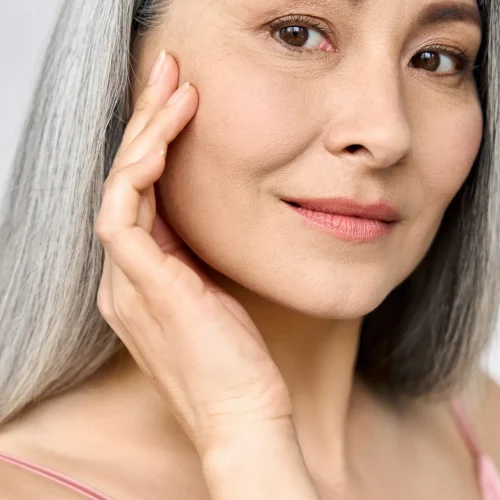 Senior older middle aged Asian woman's face with perfect skin. Older mature lady touching face. Advertising of dermatology cosmetology salon spa procedures skincare. Vertical portrait.